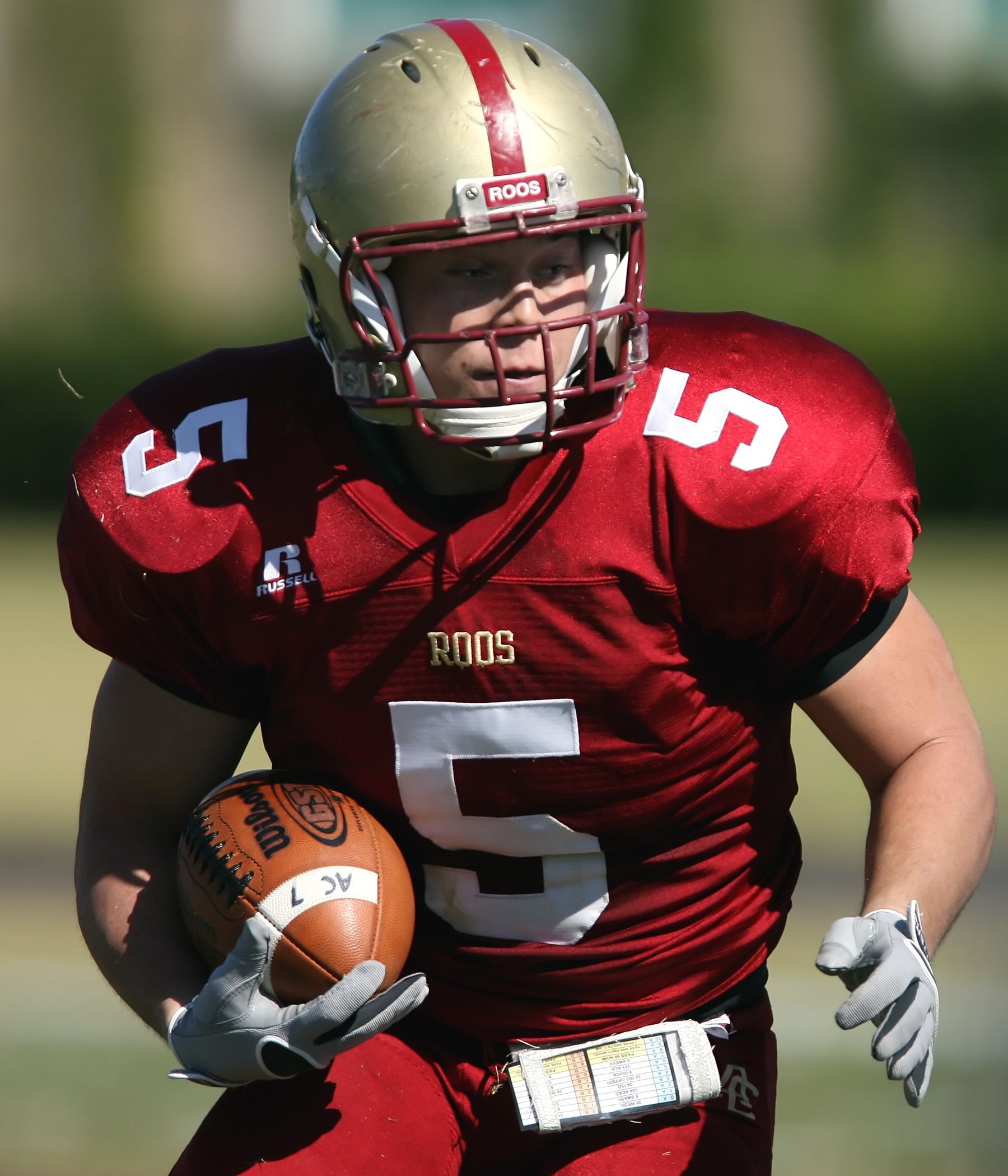 A football player in red uniform with helmet, running with ball during a game.