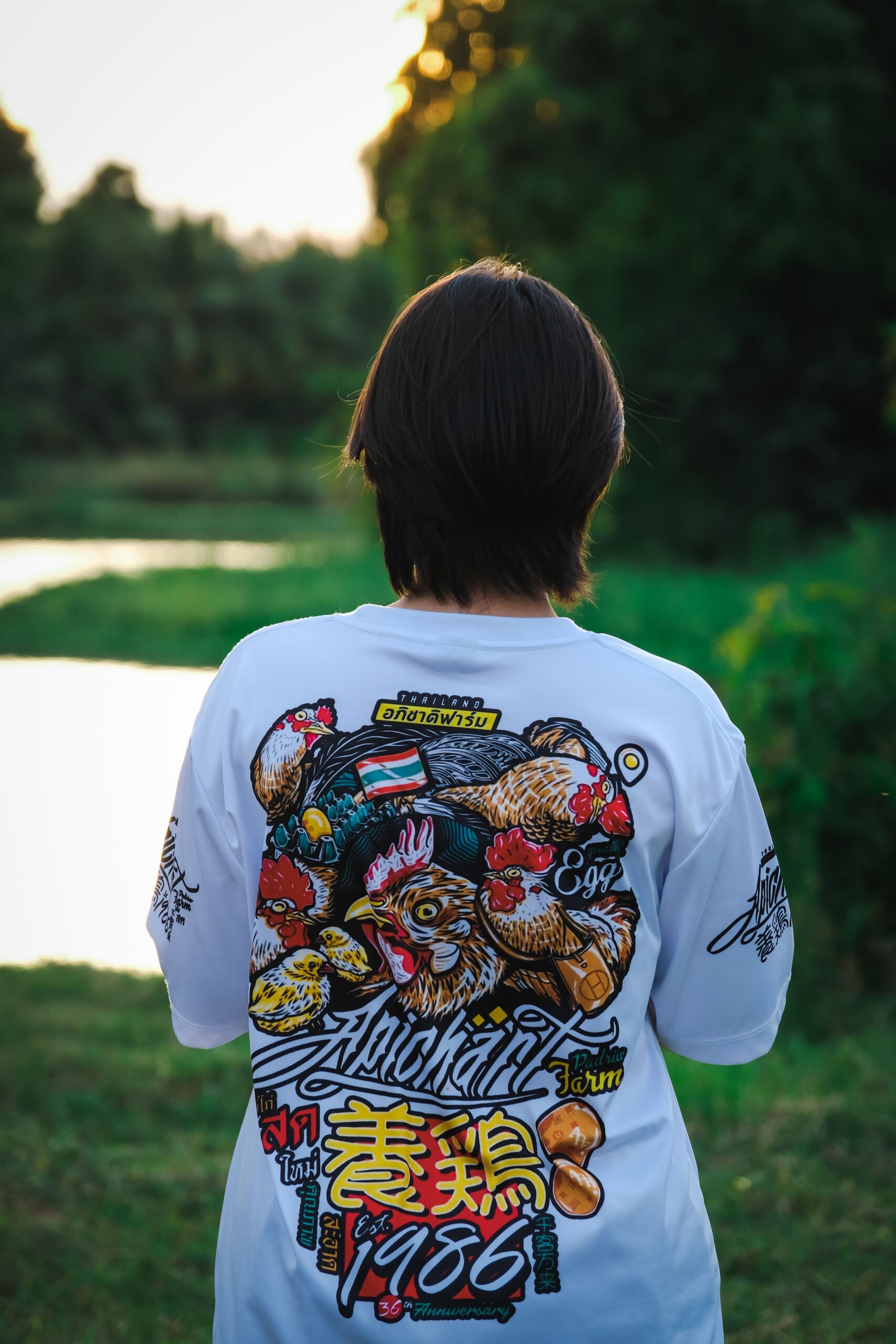 A young person with a graphic t-shirt stands near a tranquil lake in a forest setting.