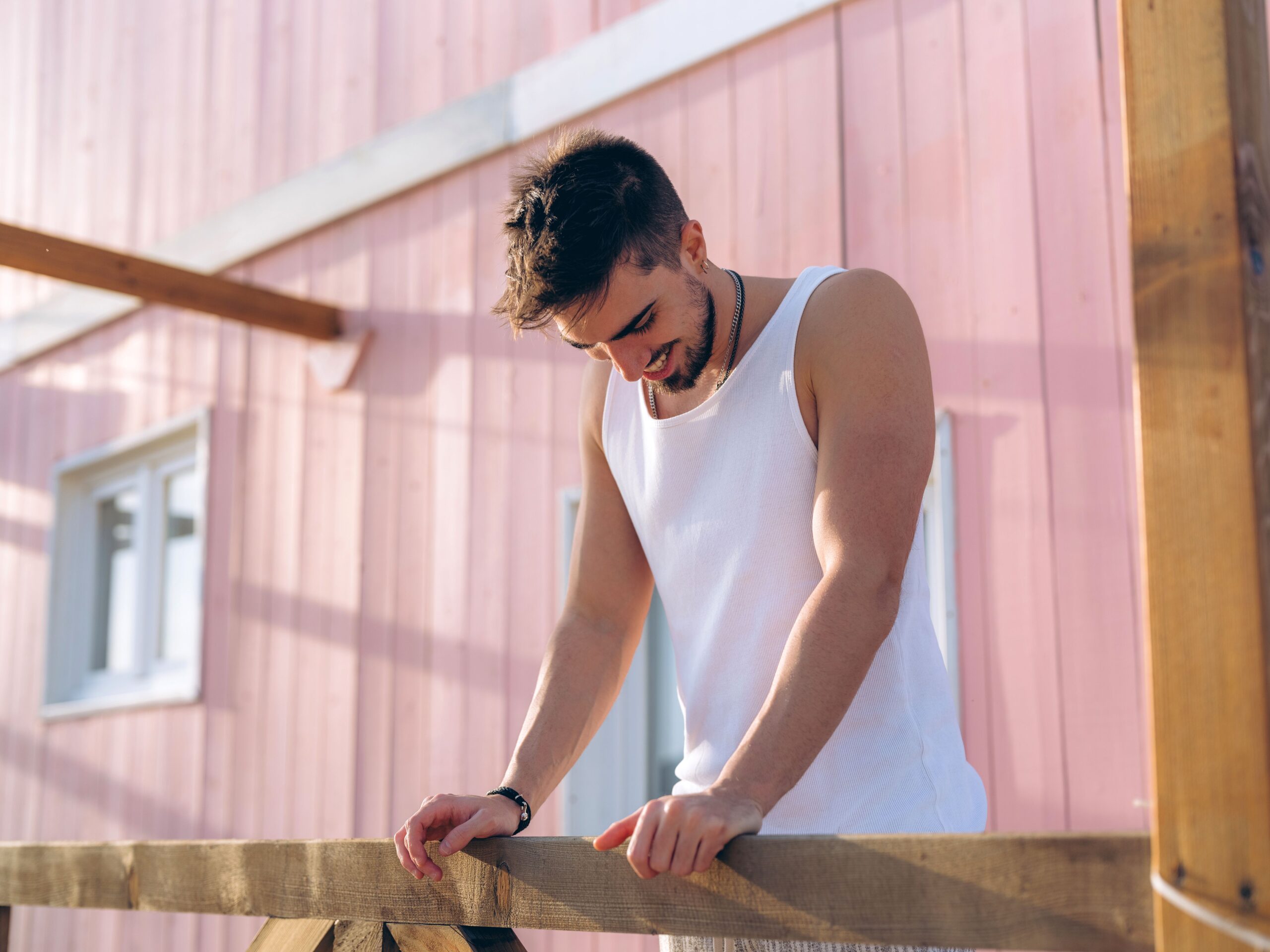 Young man smiling while leaning on a wooden railing by a pink wall in Lisbon.
