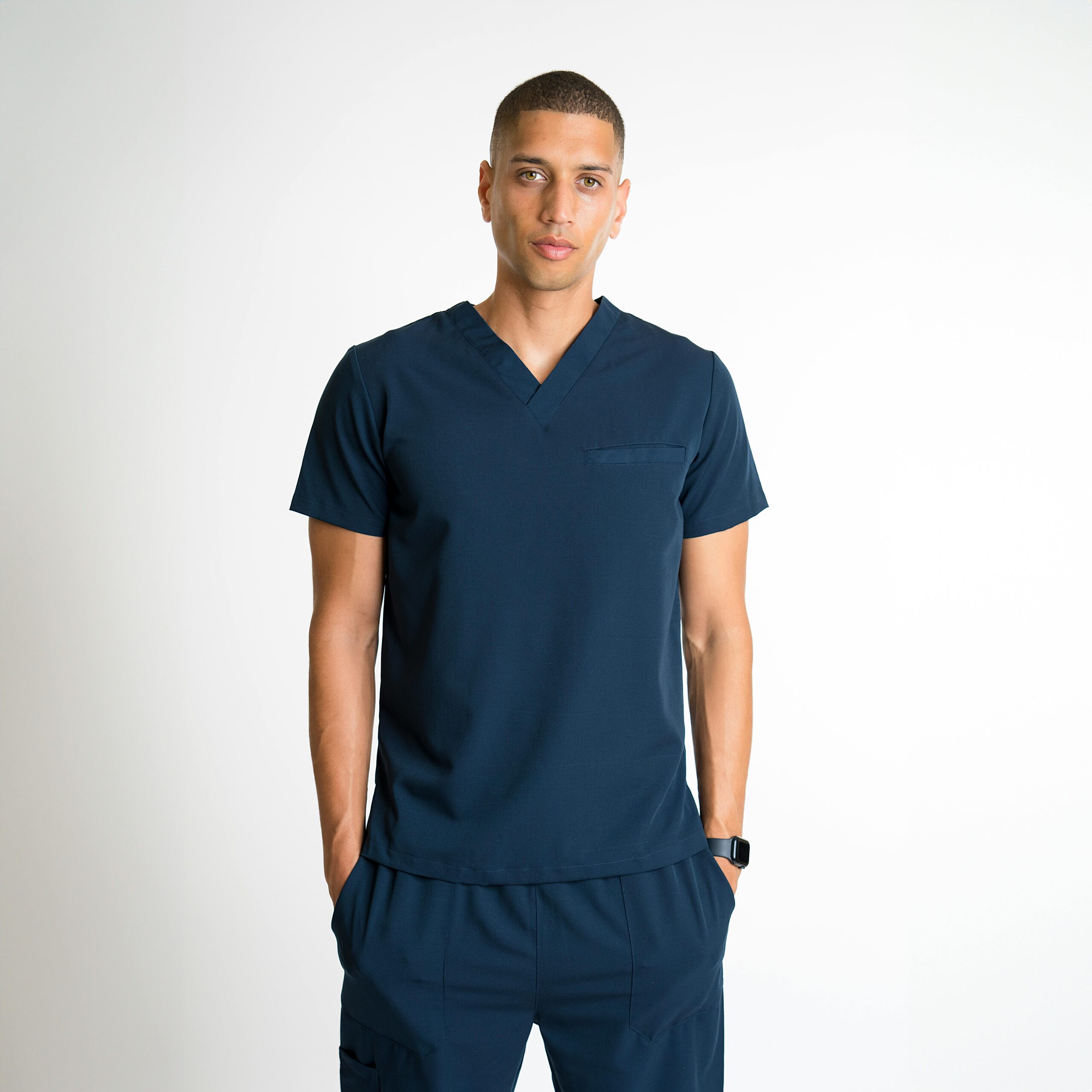 Portrait of a man wearing a dark blue t-shirt with hands in pockets, posing in a studio setting with a white background.