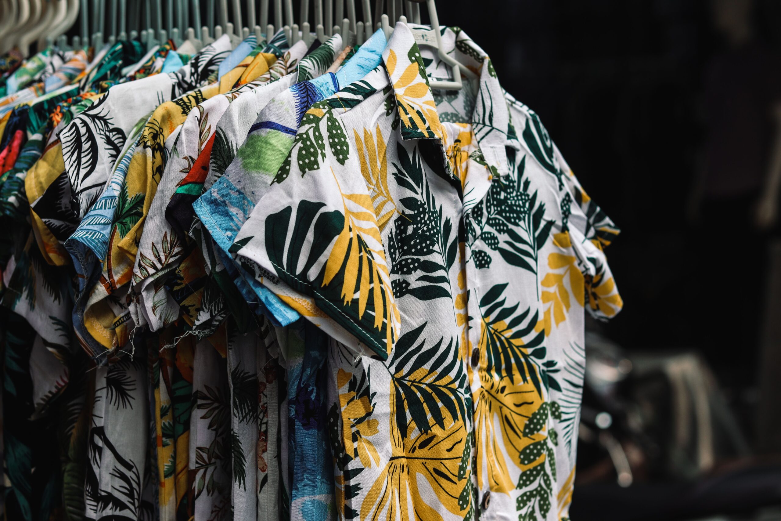 A collection of vibrant tropical print shirts hanging on a rack in a retail store.