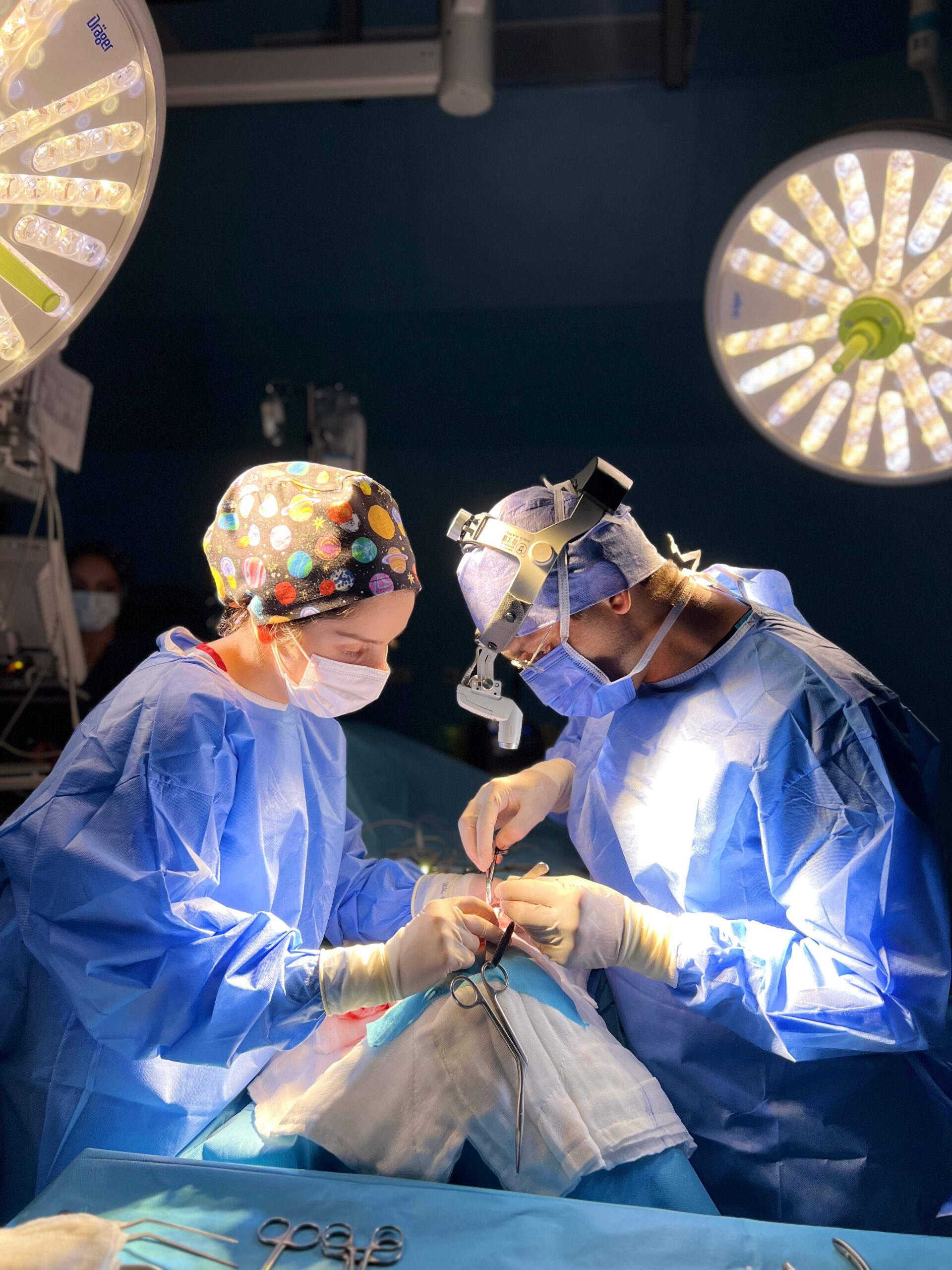 Two surgeons focused on a procedure under bright surgical lights in a sterile operating room.