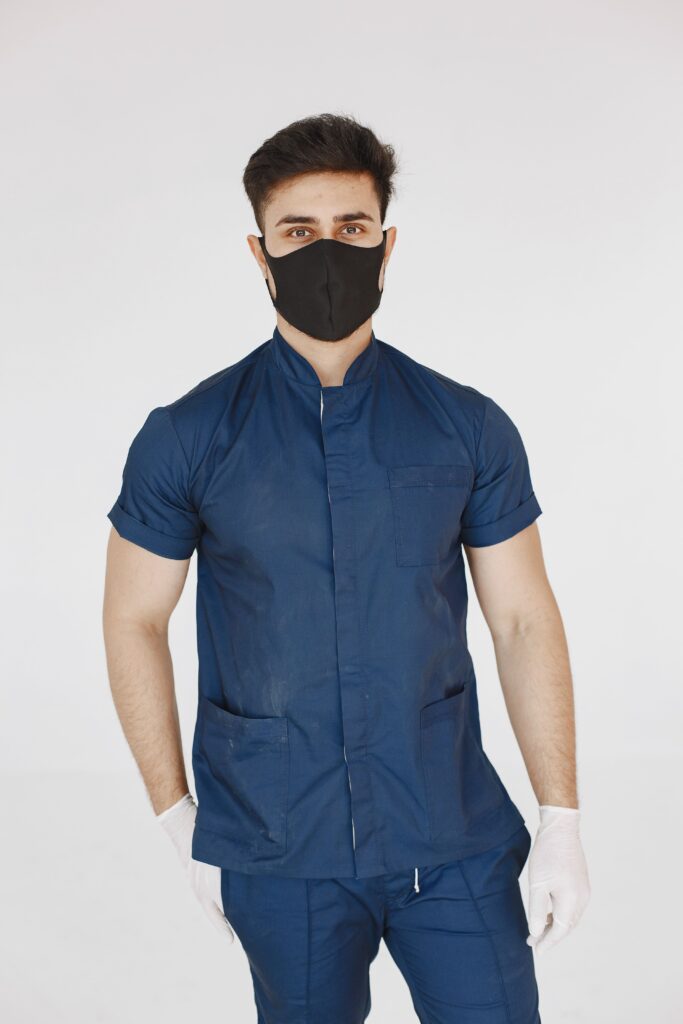 Portrait of a medical professional in scrubs with mask and gloves in studio setting.