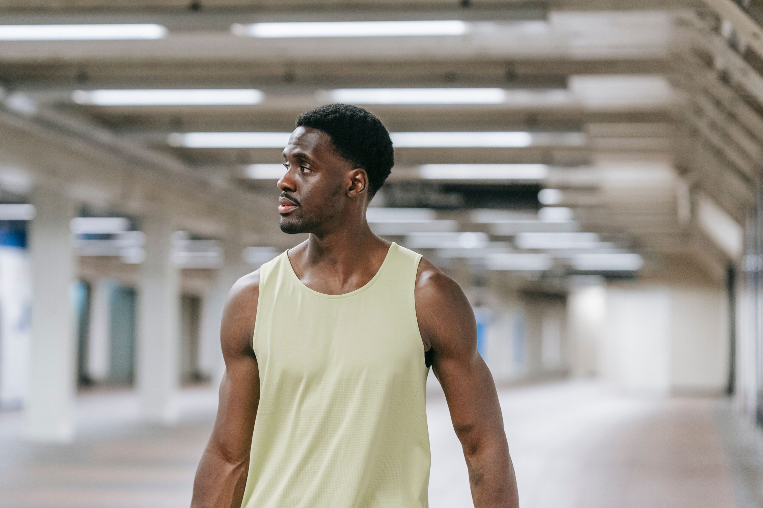 A fit man in a tank top walking in an indoor urban environment.