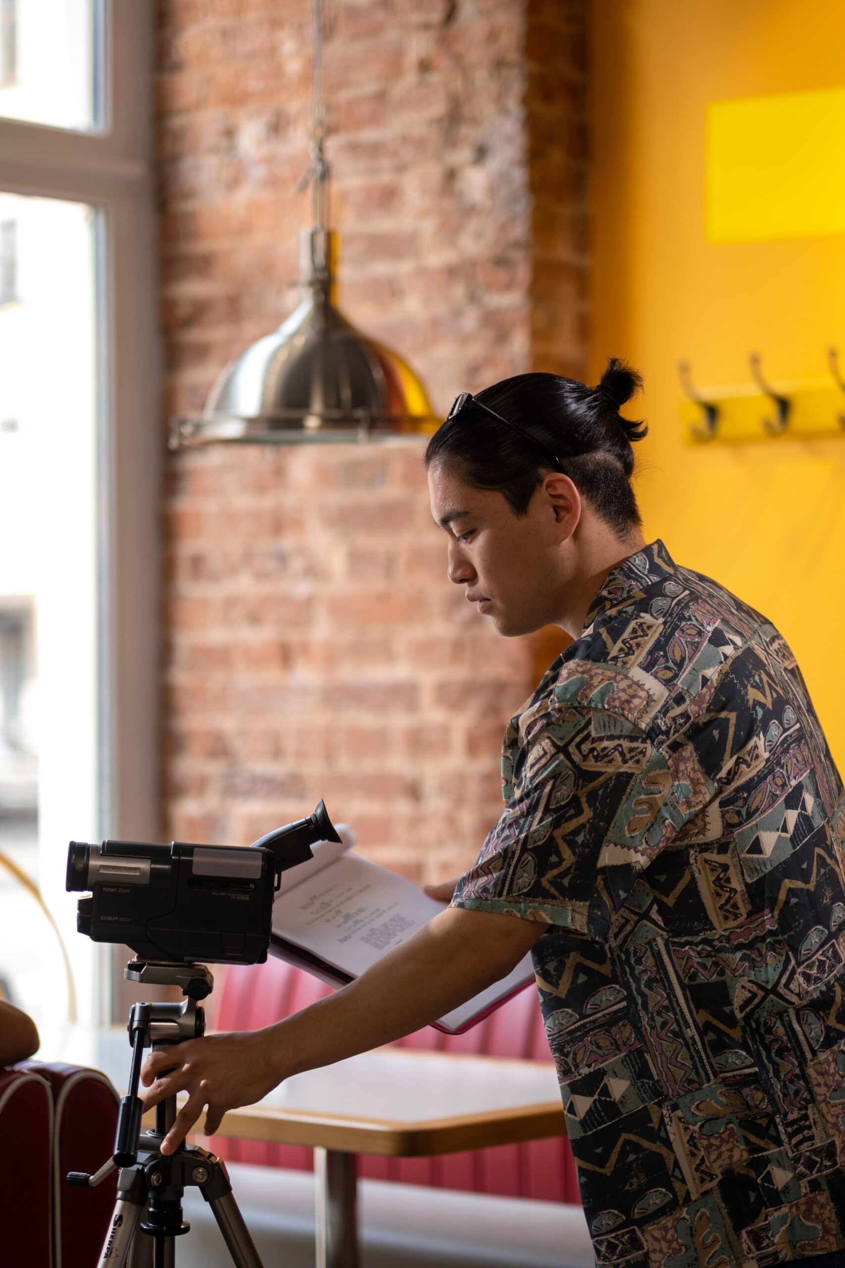 Filmmaker adjusting vintage camera on tripod in cozy indoor setting.