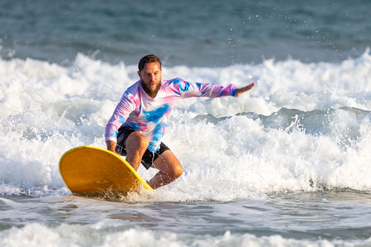 Bearded man surfing on the ocean waves with a vibrant yellow surfboard.