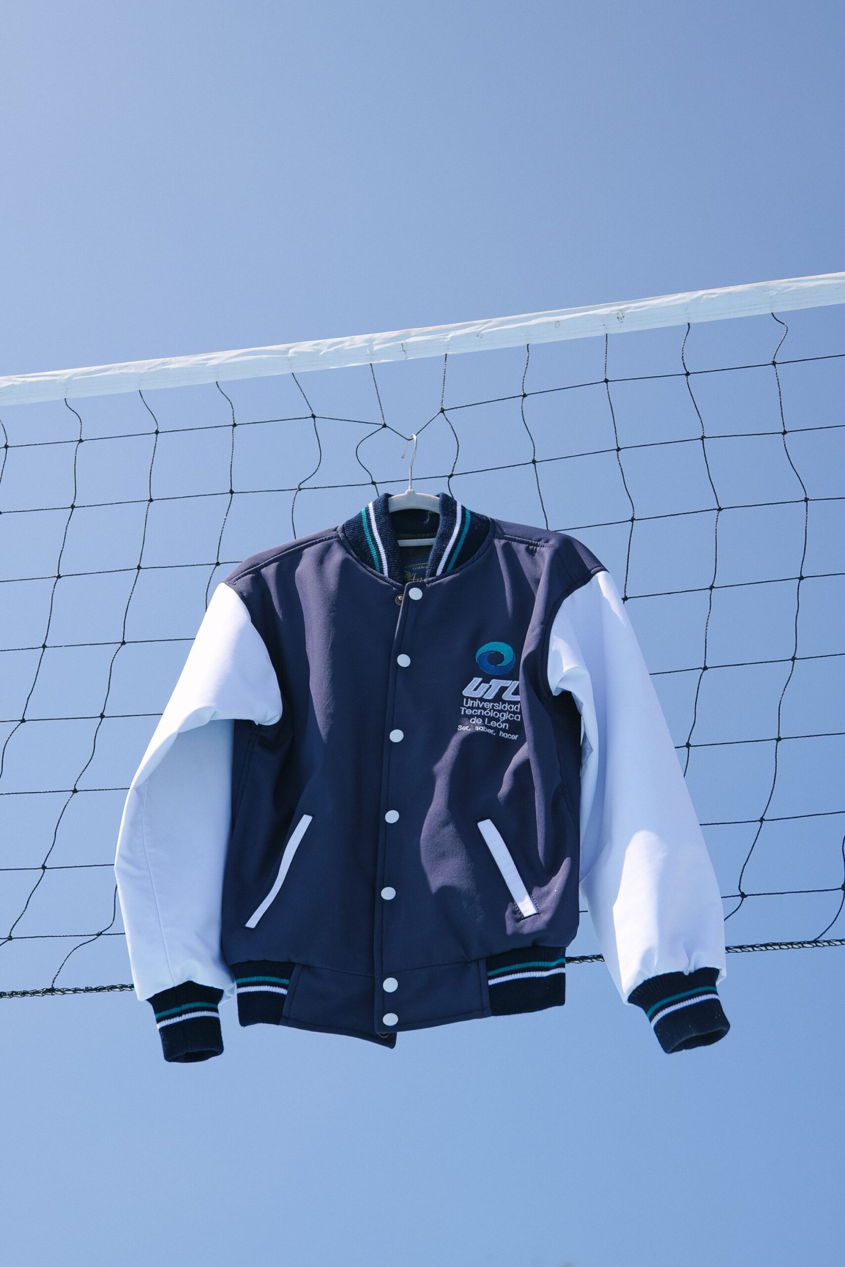 A classic varsity jacket hanging on a volleyball net against a clear blue sky in León, México.