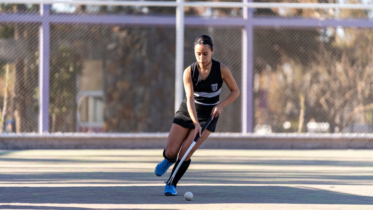Female field hockey player skillfully maneuvers the ball during a game on an outdoor court.