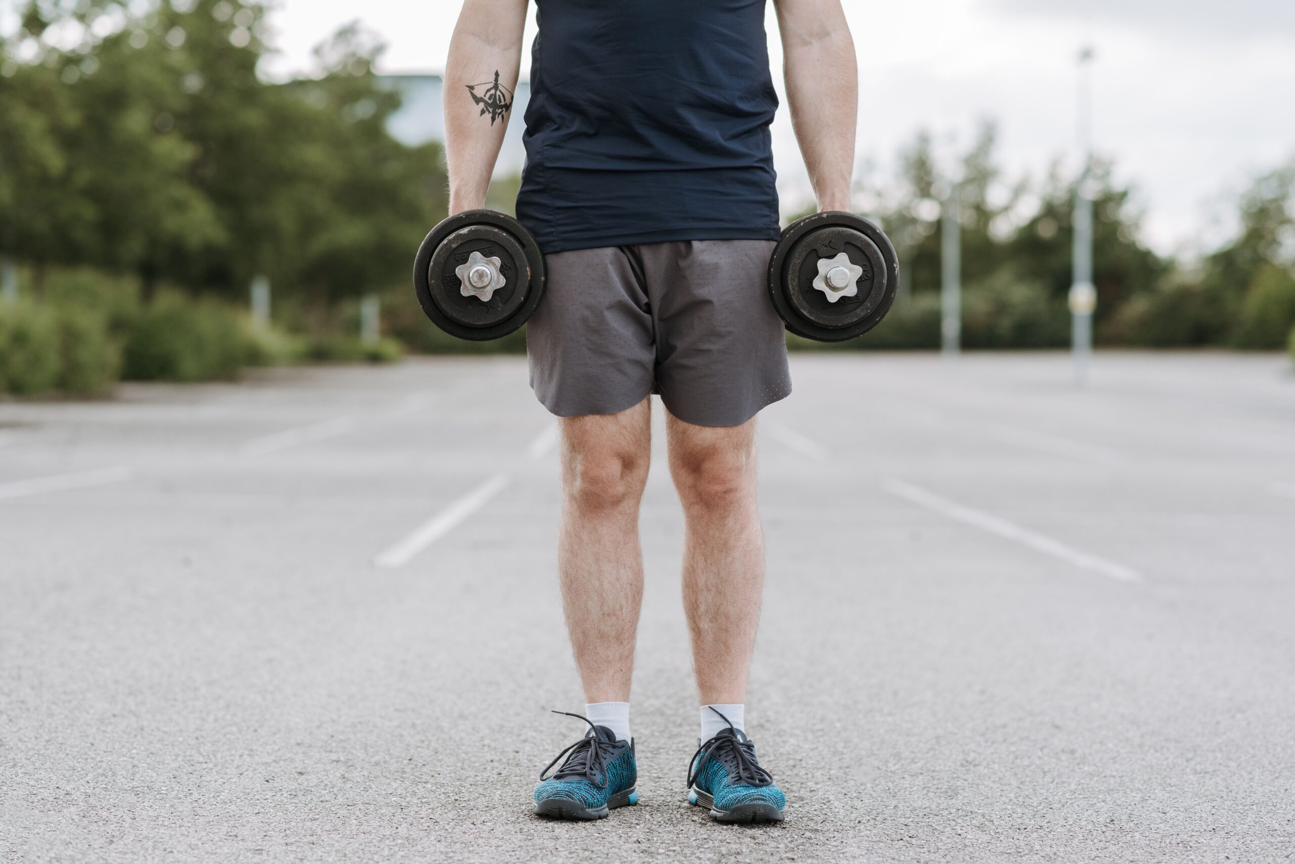 Crop unrecognizable male training with heavy dumbbells becoming stronger while working on body