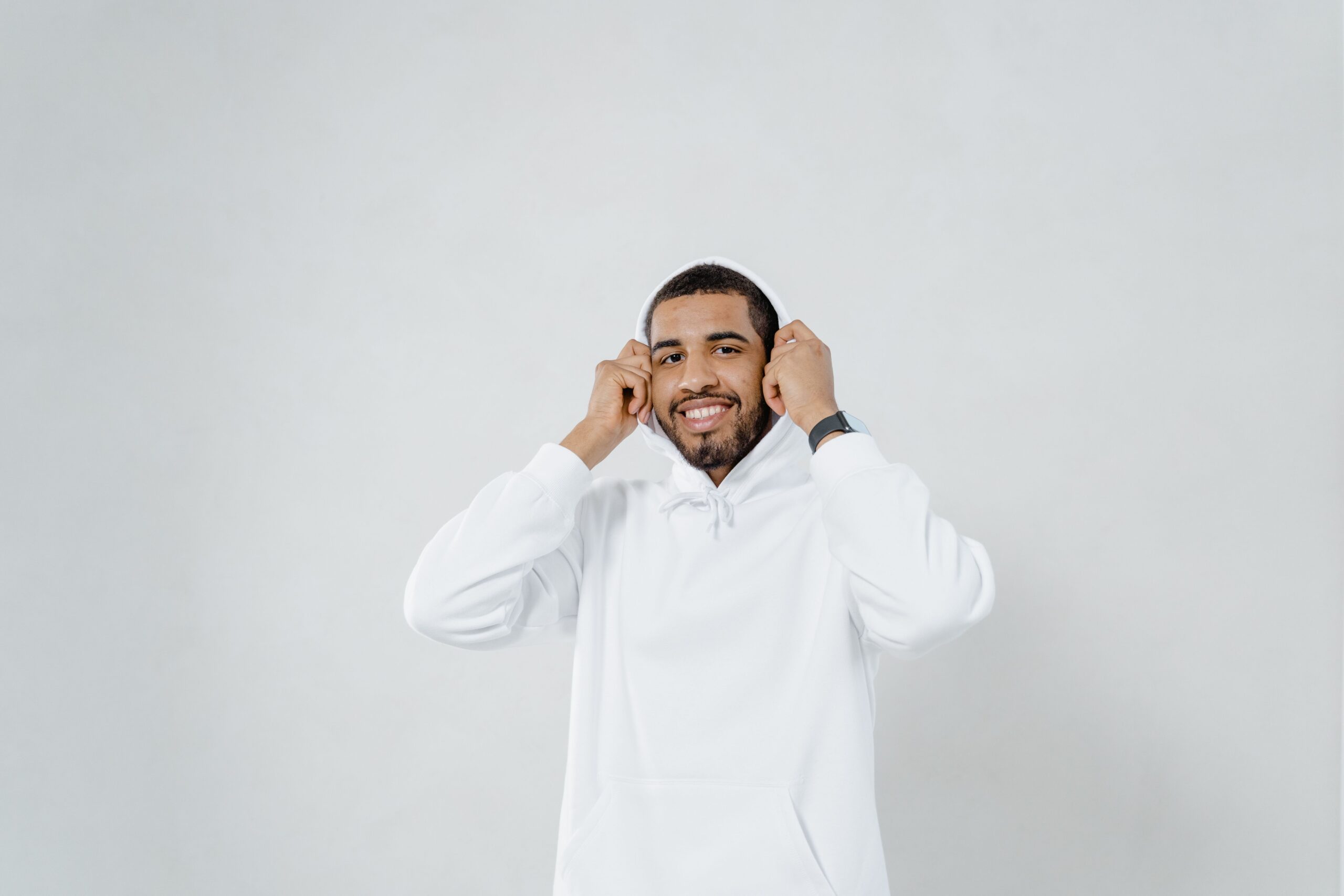 Smiling man with beard and mustache wearing a white hoodie in studio setting.