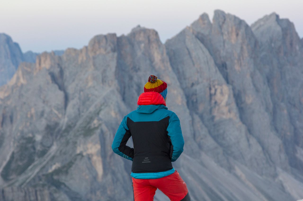 A person in colorful outdoor apparel faces majestic rocky mountains, capturing the spirit of adventure.
