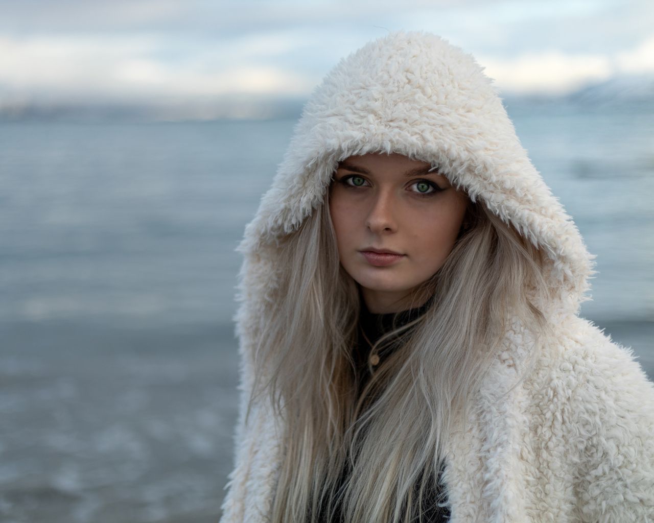 A serene winter portrait of a woman in a hooded furry coat by the sea in Lødingen, Nordland, Norge.