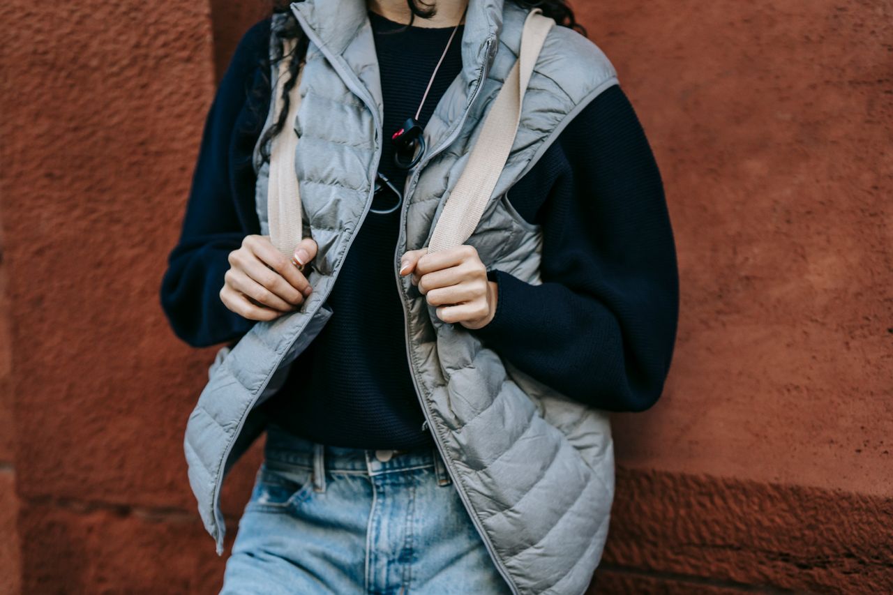 Crop unrecognizable female in trendy outfit and backpack leaning on stone wall while resting alone on street
