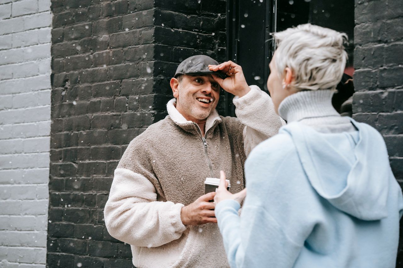 Content male in warm clothes with coffee to go speaking with anonymous female beloved while looking at each other outdoors
